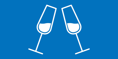 A modern hotel room with two neatly made twin beds, a wall-mounted TV, a desk with a chair, and a large window overlooking a city at night. The room has wooden floors, gray and white decor, and soft lighting from a bedside lamp.