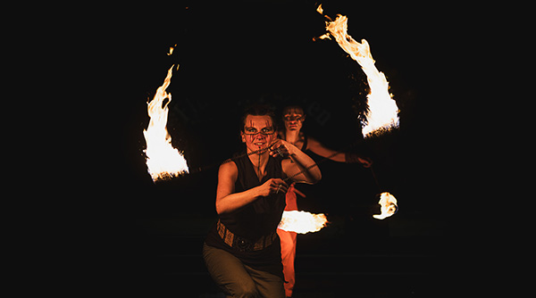 A modern hotel room with two neatly made twin beds, a wall-mounted TV, a desk with a chair, and a large window overlooking a city at night. The room has wooden floors, gray and white decor, and soft lighting from a bedside lamp.